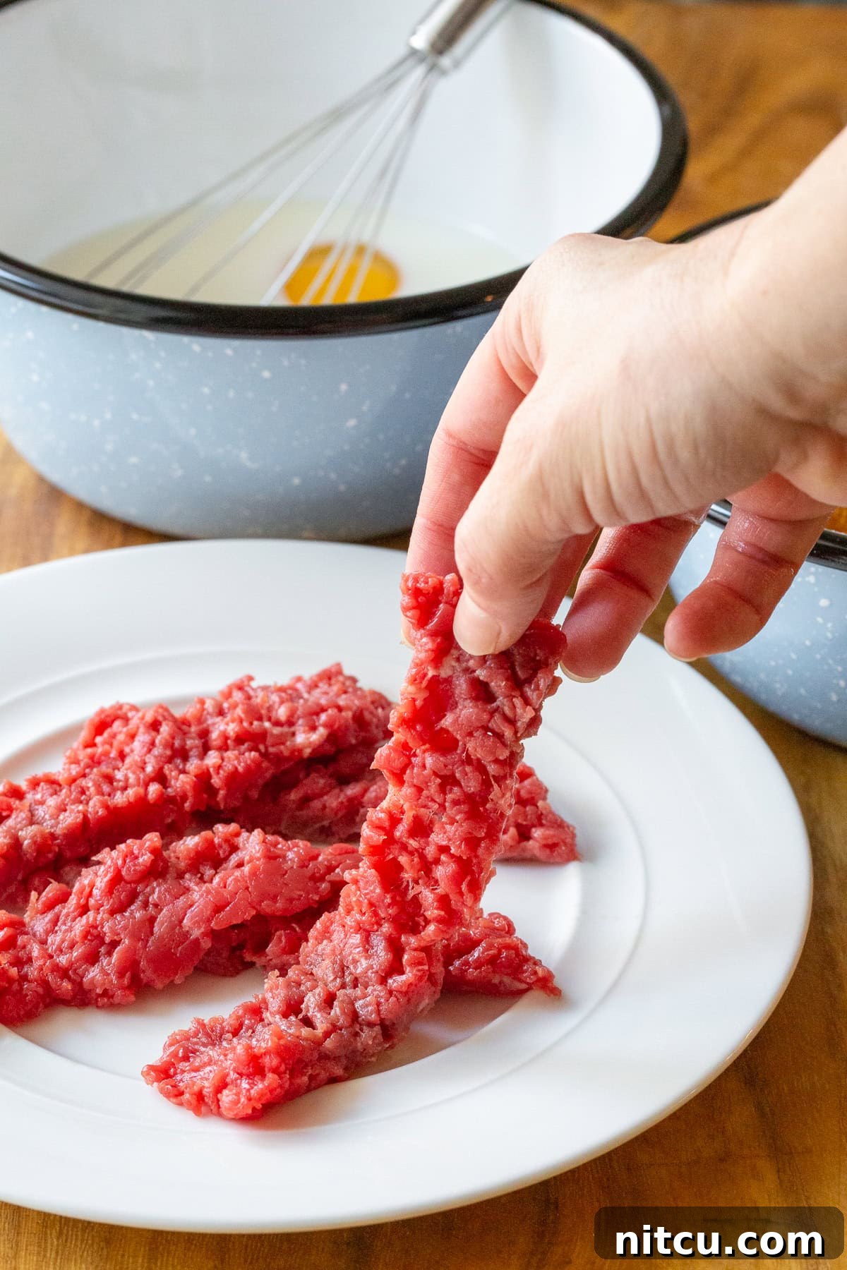 Beef Tenders 3 A hand holding a piece of raw cube steak before being breaded for steak fingers.
