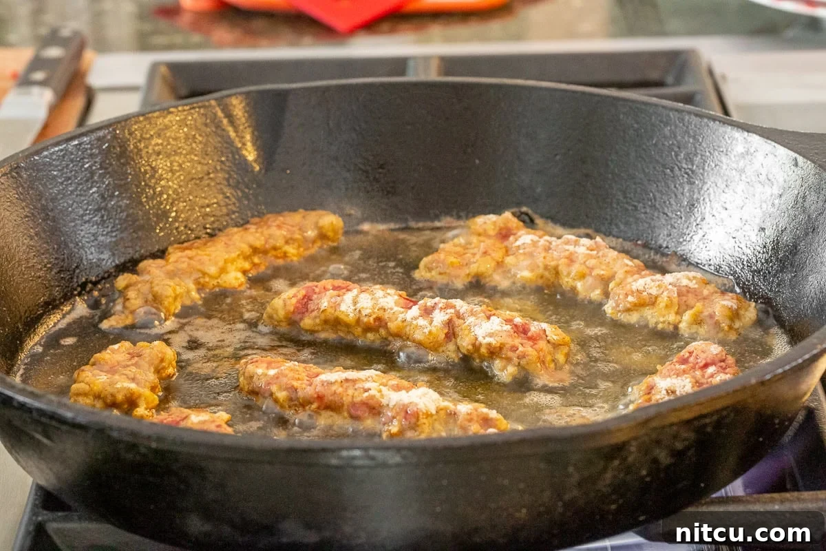 Beef Tenders 5 Several crispy steak fingers frying in a hot cast iron skillet, golden brown and bubbling.