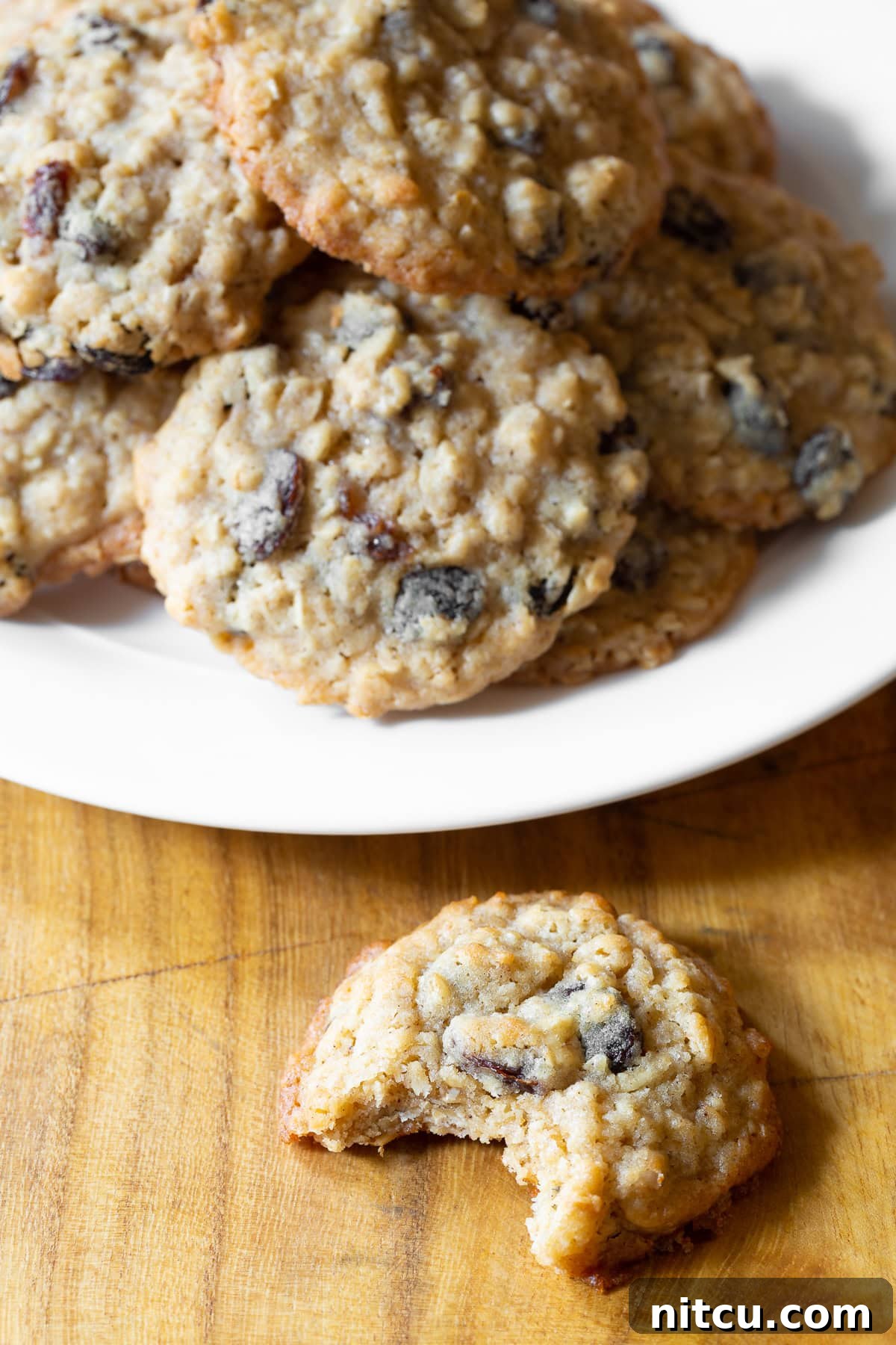 A plate full of these soft and chewy oatmeal raisin cookies recipe. A cookie with a bite taken out of it is placed in front.