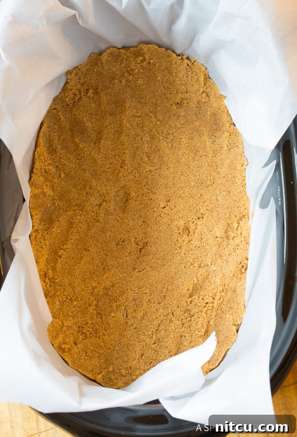 A top-down view of a golden brown graham cracker crust, perfectly pressed into the bottom of a slow cooker, ready for the cheesecake filling.