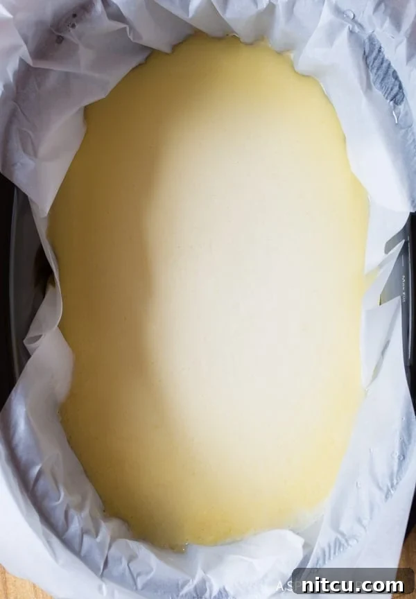 A top-down view of the uncooked cheesecake filling neatly poured over the graham cracker crust in a slow cooker, ready for baking.