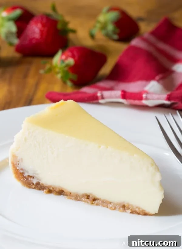 A perfectly sliced piece of slow cooker cheesecake on a white plate, with a scattering of fresh strawberries in the background, ready for serving.