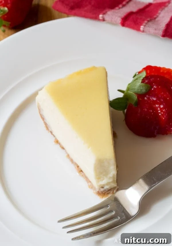 A top-down shot of a delicious slice of slow cooker cheesecake on a white plate, with a bite taken out, showing its creamy interior. A fork and a fresh strawberry sit next to the slice, inviting indulgence.
