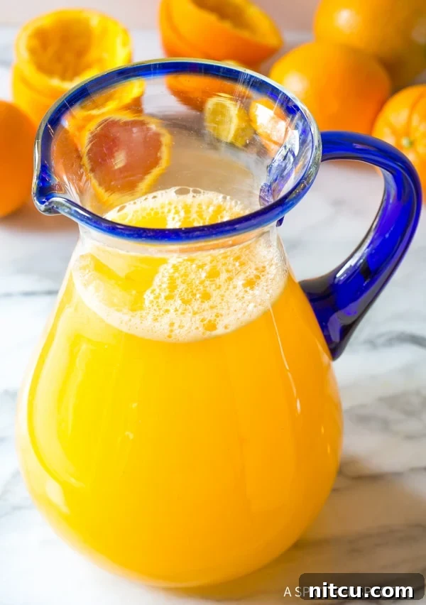 Homemade Orangeade Pitcher - Fresh Southern Summer Drink Recipe Vibrant Orangeade in a glass pitcher, surrounded by fresh oranges and a hint of lush greenery, evoking a perfect summer day.