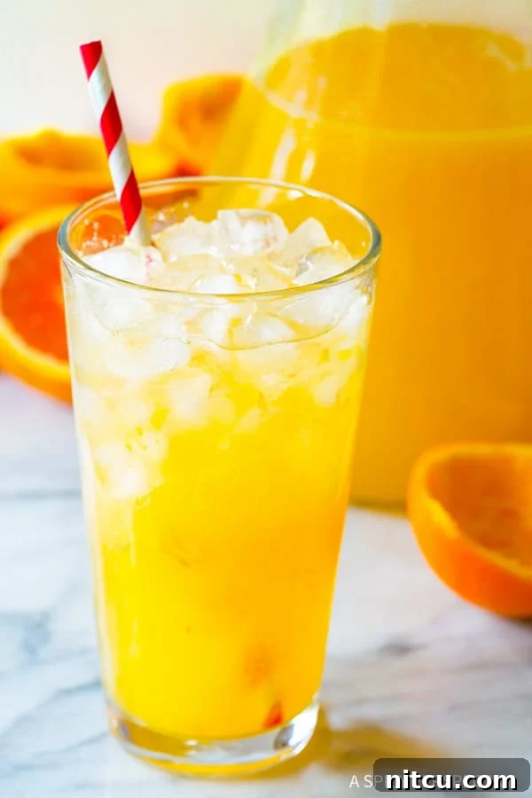 Refreshing Homemade Orangeade - Perfect Summer Drink A tall pint glass filled with ice and fresh Orangeade, adorned with a red and white striped straw, ready for sipping.