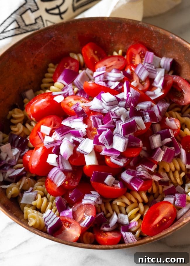 Close-up of fresh cherry tomatoes and basil, key ingredients for a vibrant pasta salad.
