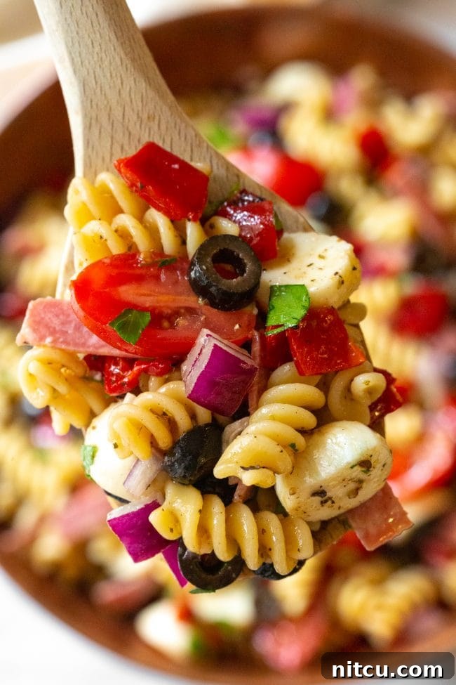 A wooden spoon with a scoop of Italian pasta salad, highlighting the texture and mix of ingredients.