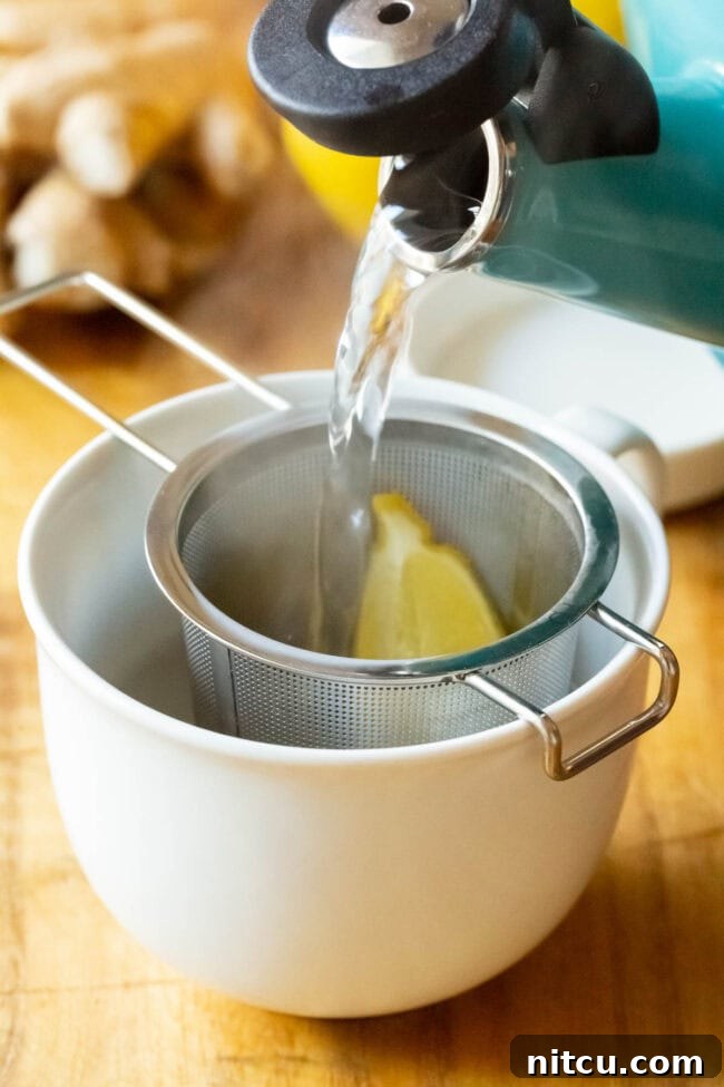Sunshine Ginger Elixir 9 A clear mug showing hot water being poured over lemon and grated ginger held in a tea infuser, creating a vibrant yellow hue.