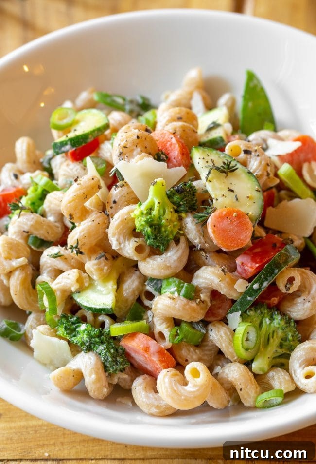 Light & Vibrant Primavera Pasta 2 A beautifully presented white bowl of skinny pasta primavera, garnished with fresh zucchini, carrots, broccoli, red peppers, and a sprinkle of shaved parmesan cheese.