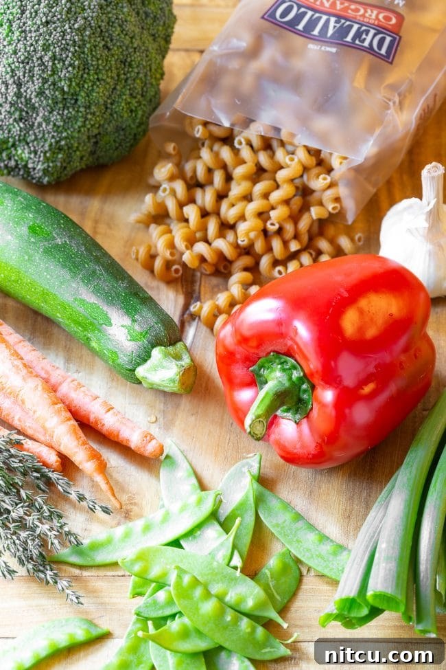 Light & Vibrant Primavera Pasta 4 A collection of fresh recipe ingredients laid out: a whole red bell pepper, fresh zucchini, vibrant carrots, crisp snow peas, green onions, raw spiral pasta (fusilli), and a bulb of garlic.
