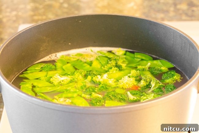 Light & Vibrant Primavera Pasta 5 A large pot of boiling water with broccoli florets, snow peas, and sliced carrots, showing the blanching process.