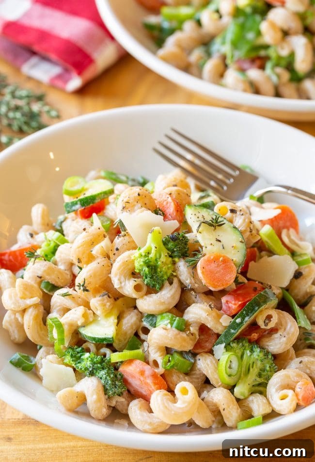 Light & Vibrant Primavera Pasta 9 A white bowl of creamy noodles, generously mixed with chopped zucchini, carrots, broccoli, red peppers, and finished with shaved parmesan cheese.