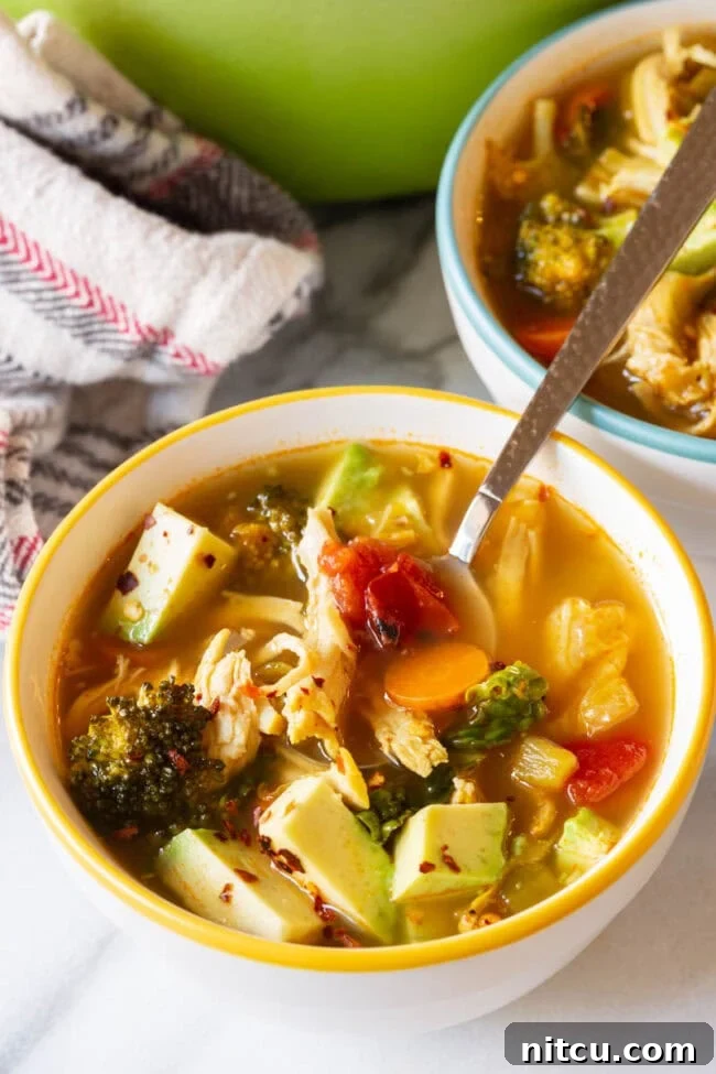 Bowl of chicken vegetable soup with a silver spoon.