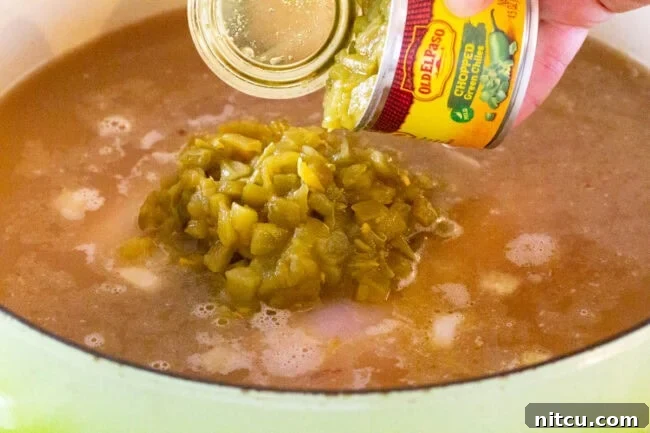 Hand pouring a can of green chiles into a pot of soup.