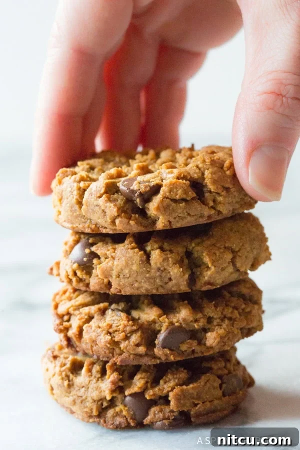 Magic 4-Ingredient Guilt-Free Chocolate Chip Cookies 3 Hand reaching for a top cookie from a stack of four mouth-watering peanut butter chocolate chip cookies.