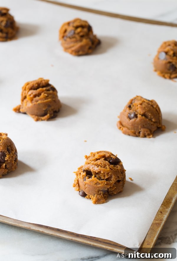 Magic 4-Ingredient Guilt-Free Chocolate Chip Cookies 6 Perfectly round scoopfuls of raw cookie dough arranged on parchment paper on a baking sheet, ready for shaping.