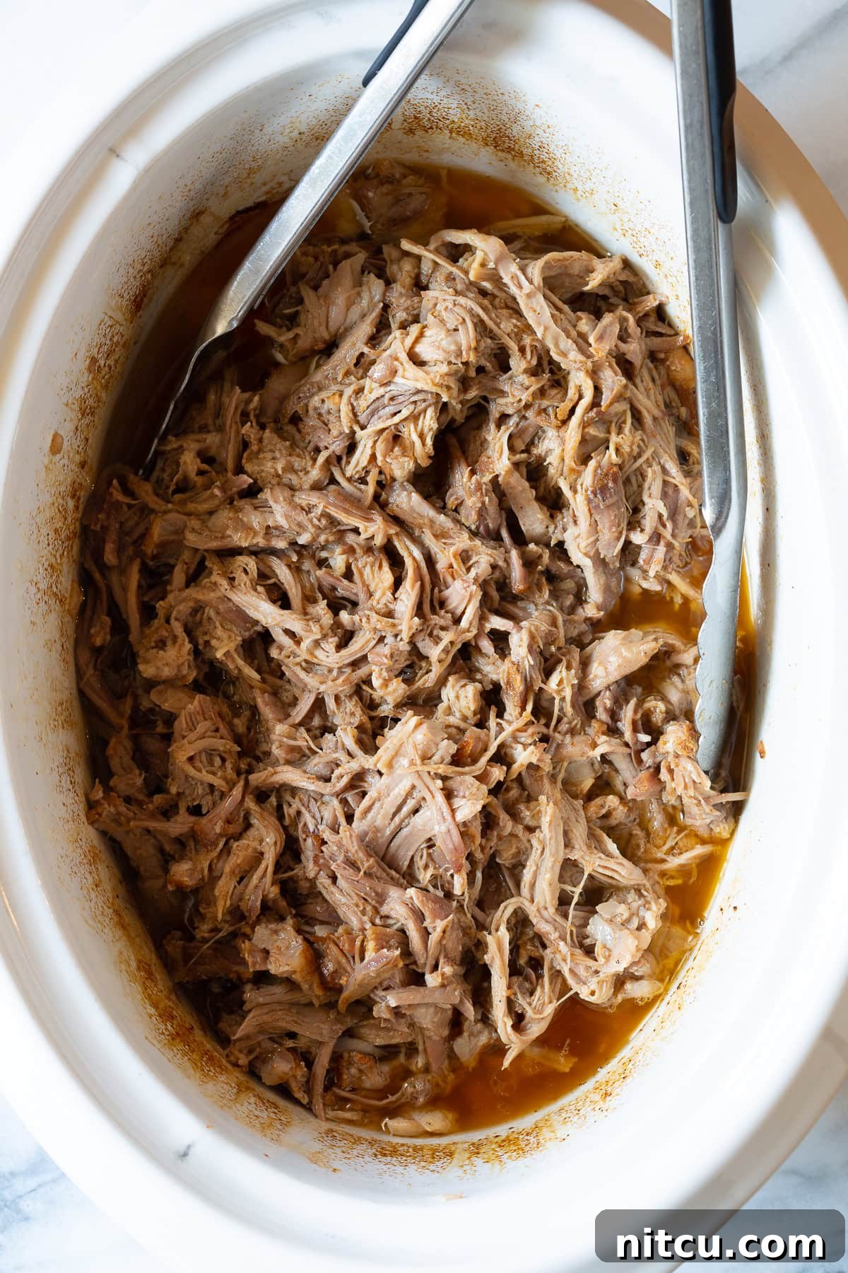 Smoky Perfection: Crockpot Pulled Pork 2 Shredded pork in the crockpot with metal tongs.
