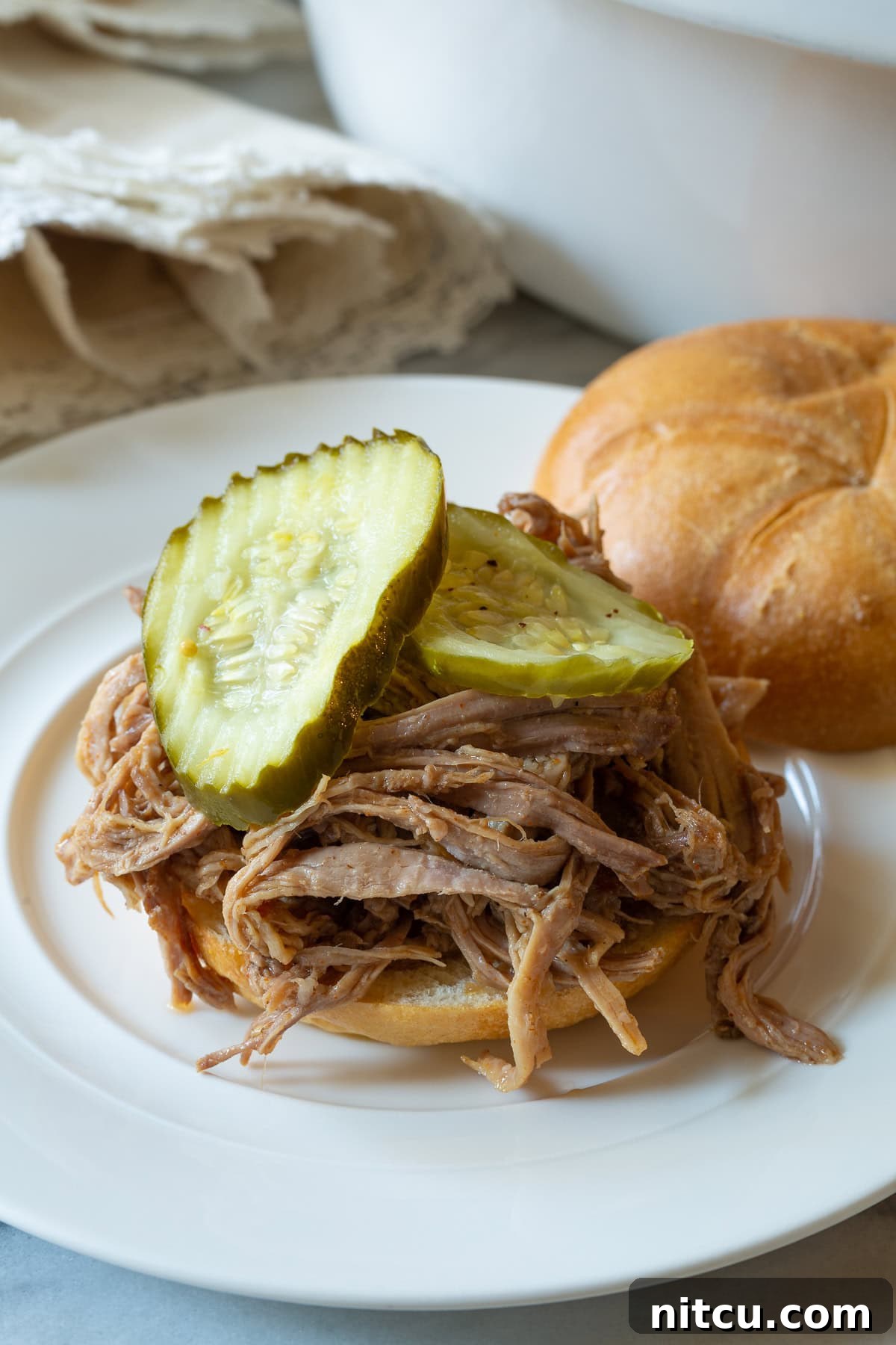Smoky Perfection: Crockpot Pulled Pork 11 Shredded smoked pulled pork on a bun with pickles.