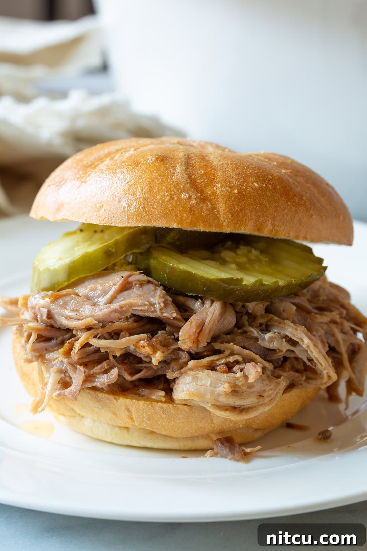 Smoky Perfection: Crockpot Pulled Pork 4 Smoked pulled pork on a bun with pickles served on a white plate.
