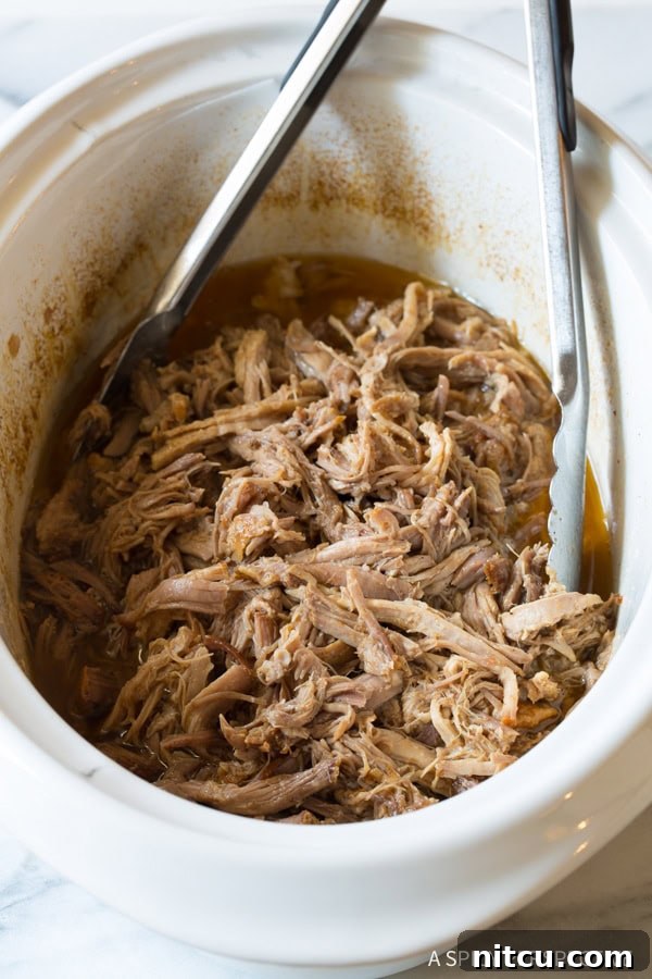 Smoky Perfection: Crockpot Pulled Pork 5 Shredded pork in the crockpot with metal tongs.