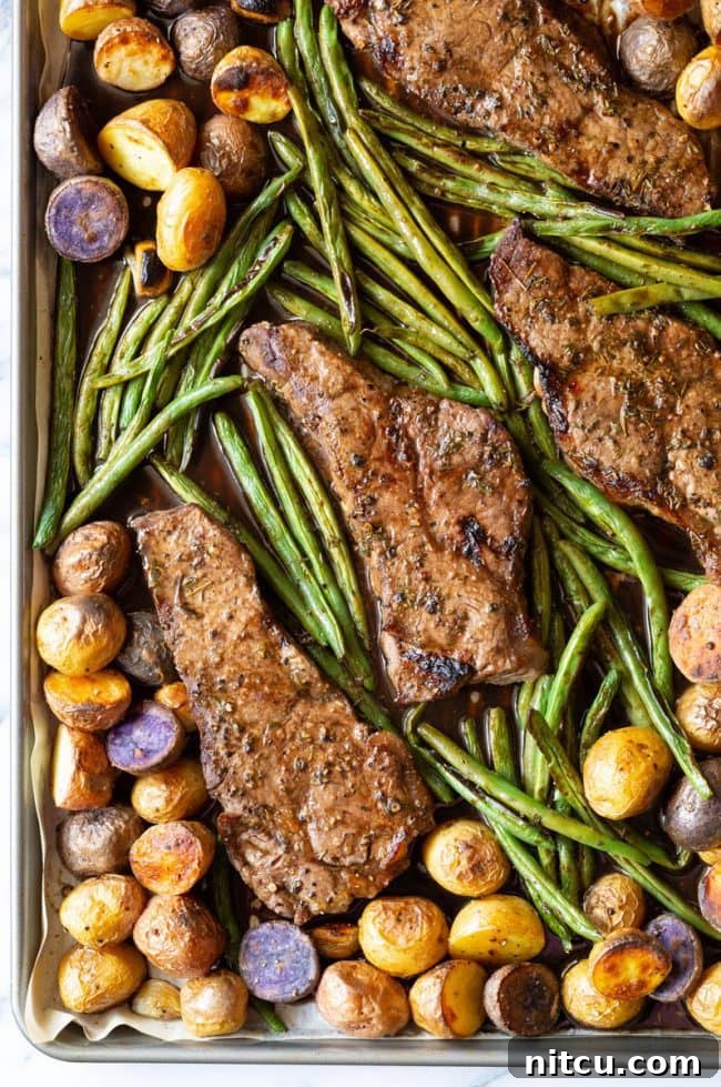 Top view of a beautifully cooked Balsamic Oven Baked Steak Sheet Pan Dinner, featuring sliced steak, golden potatoes, and vibrant green beans.