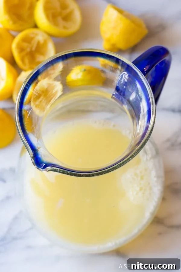 Naturally Sweet Lemonade 6 Freshly squeezed lemon juice being poured into a large, clear glass pitcher, ready for mixing.