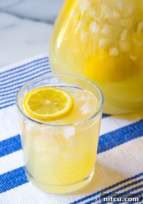 Naturally Sweet Lemonade 9 A beautifully composed image of a glass filled with ice and Stevia Lemonade, perfectly garnished with a lemon slice, placed next to a full pitcher of the beverage.