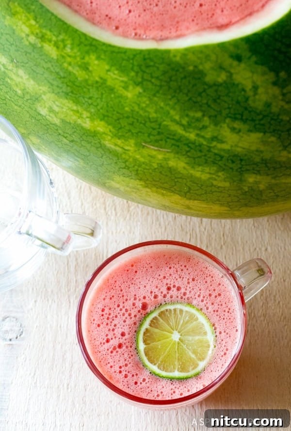 A top down view of rum punch in a glass with a lime slice next to the watermelon bowl.