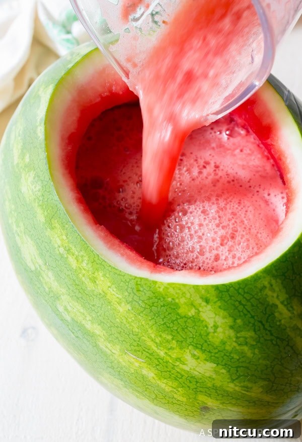 A blender pouring rum punch into the watermelon bowl.
