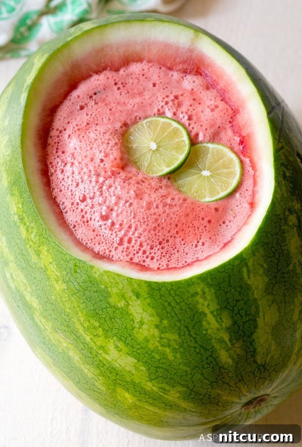 A watermelon bowl filled with rum punch and topped with two lime slices.
