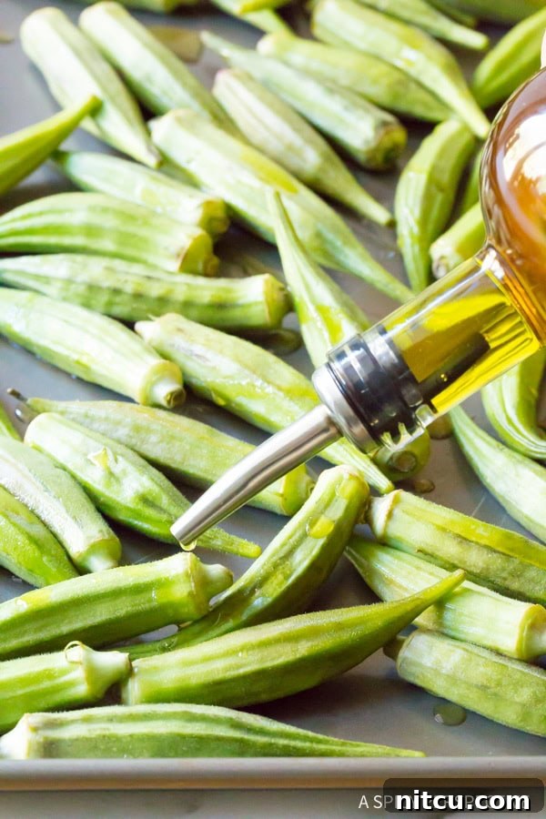 Hands preparing fresh okra with olive oil and spices on a baking sheet