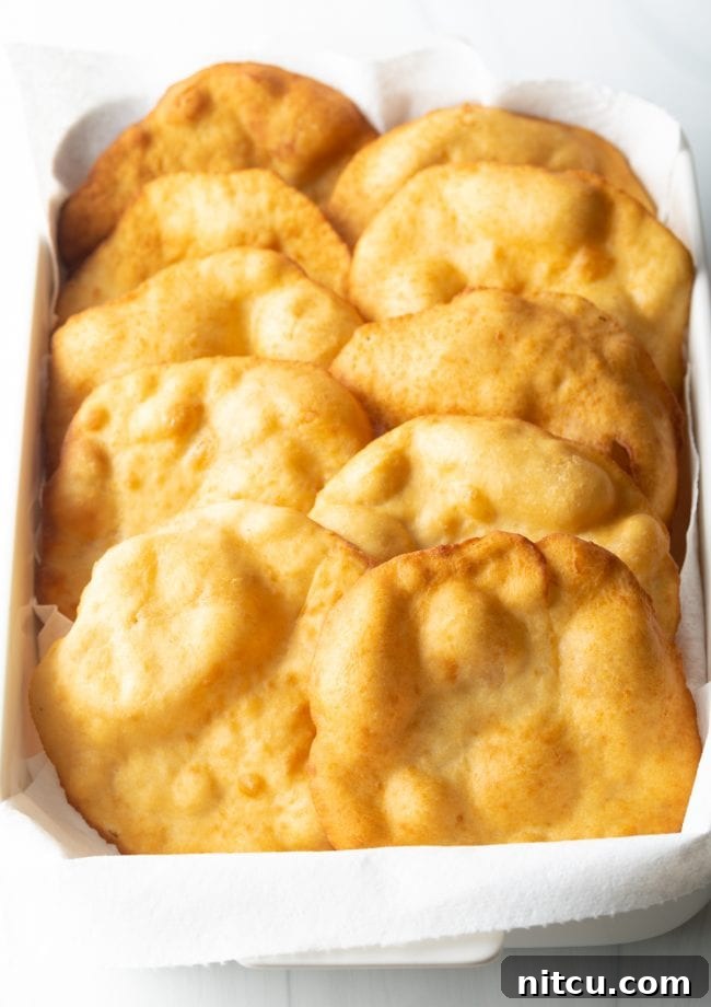 Authentic Navajo Fry Bread 11 Freshly fried Navajo fry bread stacked neatly in a baking dish lined with paper towels, draining excess oil and ready to be served or topped.