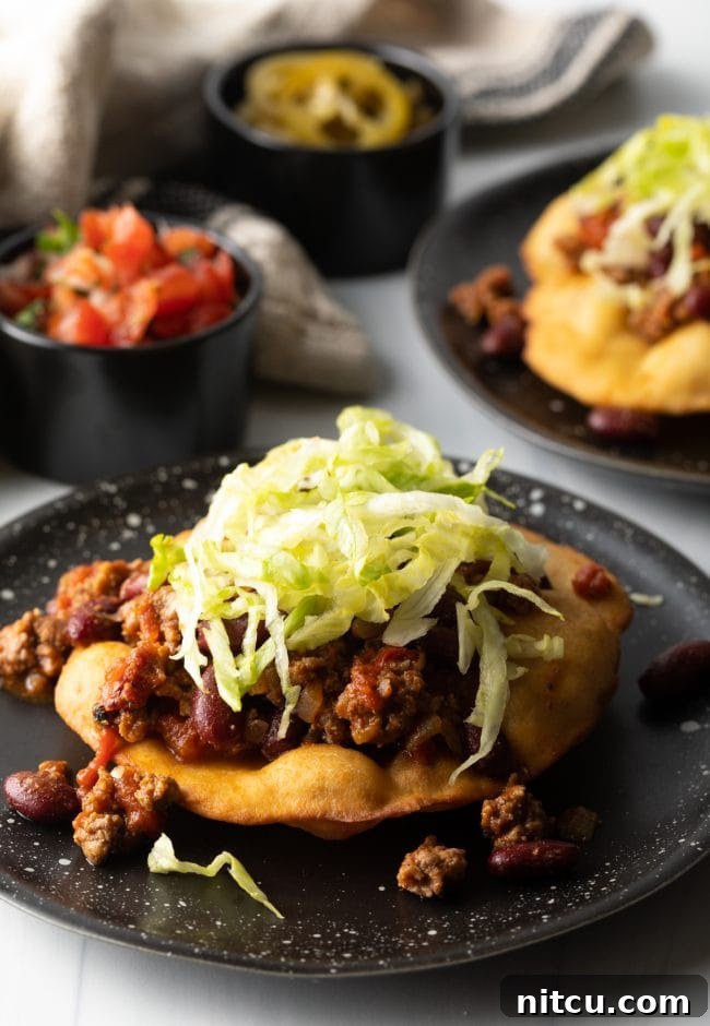 Authentic Navajo Fry Bread 14 A hand assembling a crispy fry bread taco, layering seasoned meat and fresh shredded lettuce, preparing a delicious meal.