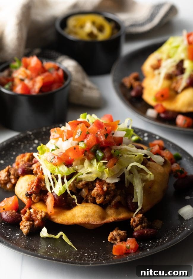 Authentic Navajo Fry Bread 15 A fully loaded Navajo fry bread taco, generously topped with seasoned ground beef, fresh lettuce, tomatoes, and other vibrant garnishes, showcasing a hearty meal.