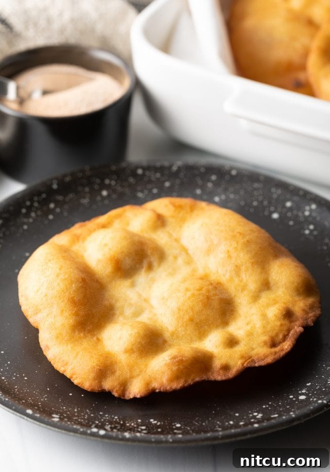 Authentic Navajo Fry Bread 16 A freshly fried, golden-brown crispy fry bread resting on a black plate, showcasing its simple beauty before adding toppings.