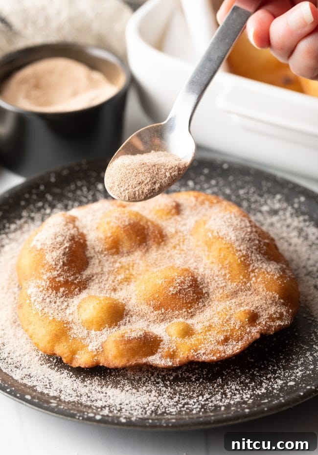 Authentic Navajo Fry Bread 17 A hand gently sprinkling a generous amount of cinnamon sugar over a warm, freshly fried Indian Fry Bread, creating a sweet dessert.