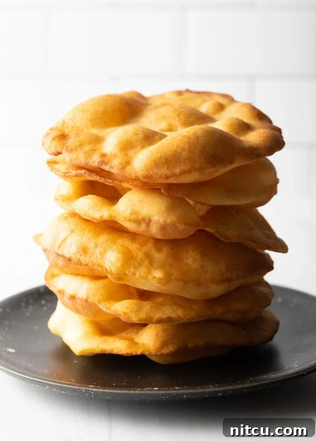 Authentic Navajo Fry Bread 3 A large stack of golden-brown Navajo fry bread, perfectly round and puffed, resting on a black plate, ready to be served or topped.