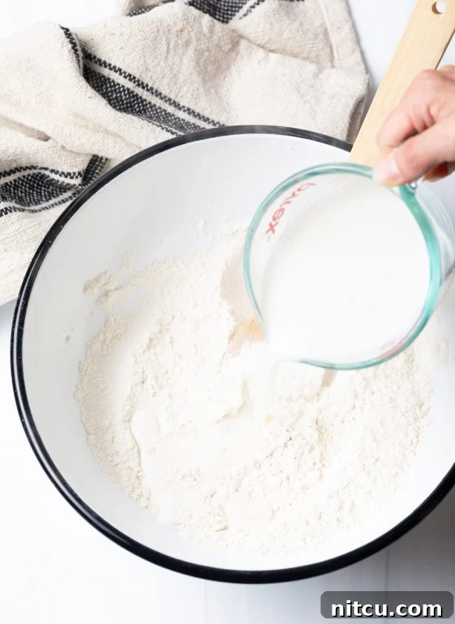 Authentic Navajo Fry Bread 5 A hand carefully pouring hot liquid (milk and water mixture) into a bowl of dry ingredients, beginning the process of mixing the fry bread dough.