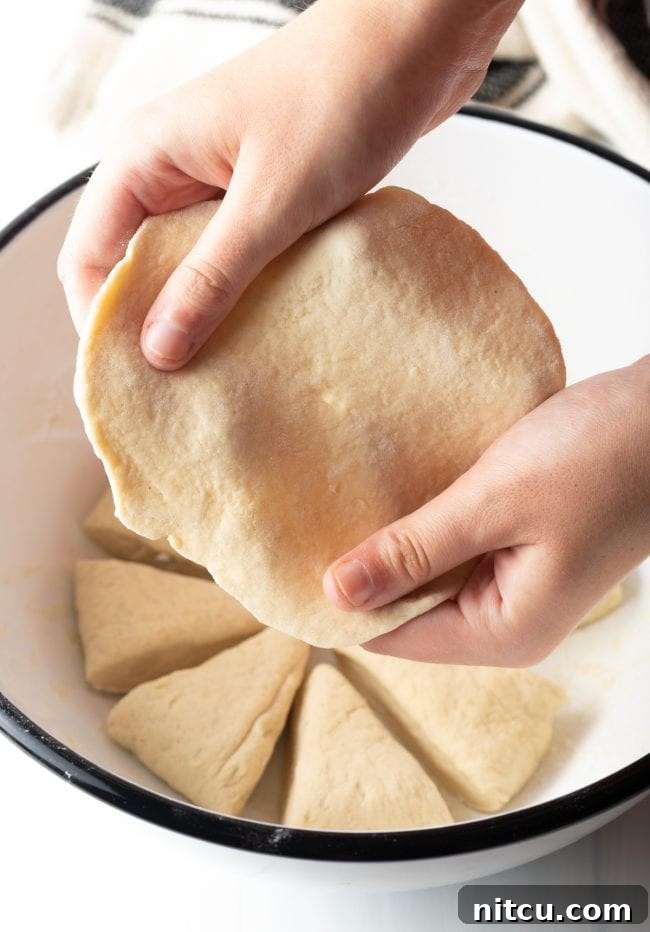 Authentic Navajo Fry Bread 8 A person gently stretching and pulling the edges of the soft dough by hand, shaping it into a thin, round tortilla-like disk, preparing it for frying.