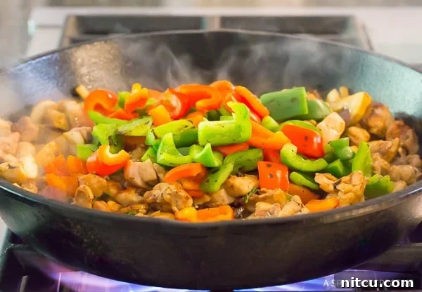 Authentic Croatian Chicken Dinner 7 Charred bell peppers being tossed back into a skillet with fully cooked chicken and other vegetables, blending flavors.