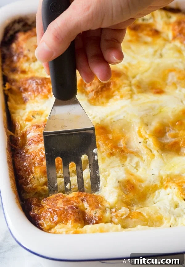 Hand using a spatula to take a serving of the strukli from a baking dish. 