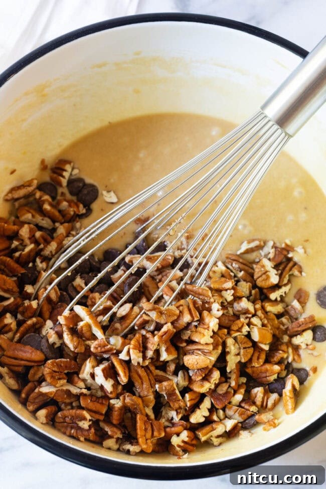 pecans Close-up of a large mixing bowl with an eggy batter, as chopped nuts and dark chocolate chips are being whisked in.