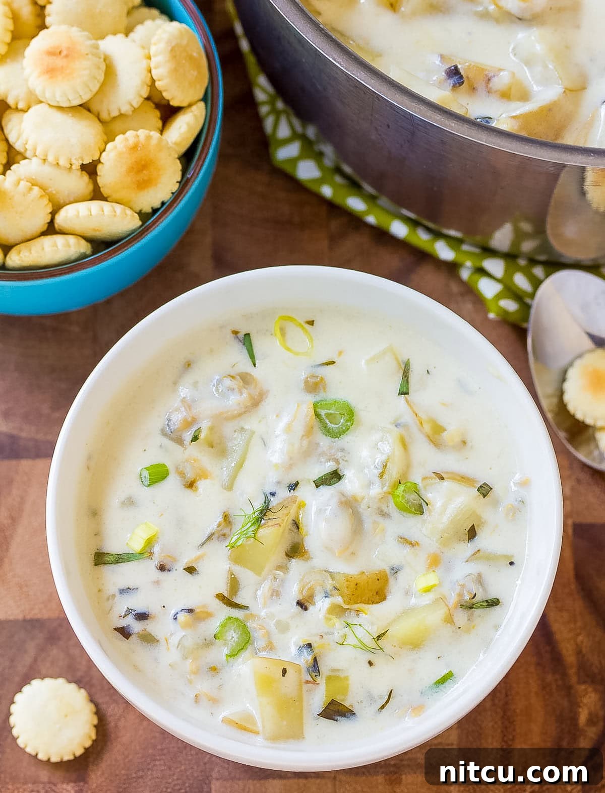 New England Clam Chowder in a bowl with crackers and scallions, garnished beautifully