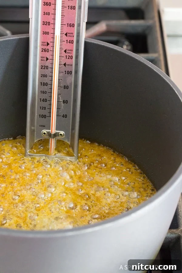 Christmas Toffee Crunch 5 Buttery brown sugar toffee mixture simmering in a saucepan with a candy thermometer showing temperature.