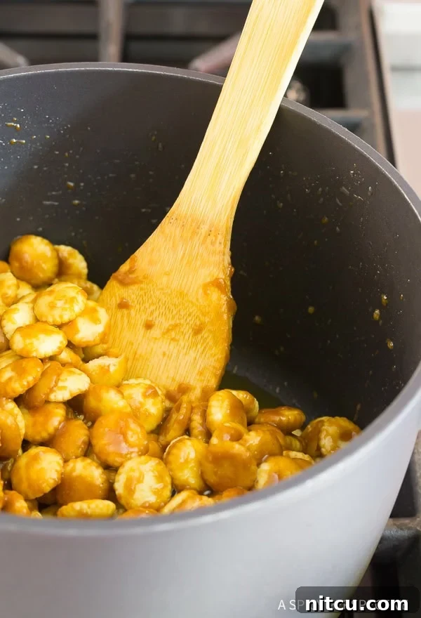 Christmas Toffee Crunch 6 A wooden spoon carefully coats oyster crackers with warm toffee mixture in a saucepan.