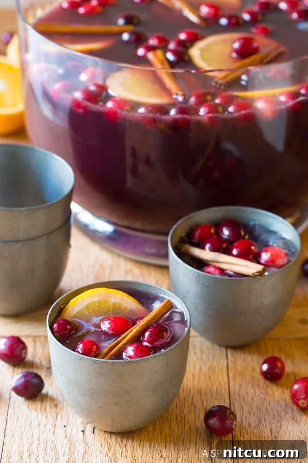 Festive Wine Medley 2 A beautiful punch bowl filled with Holiday Wine Punch, garnished with fresh cranberries and orange slices, with two elegant silver glasses ready for serving.