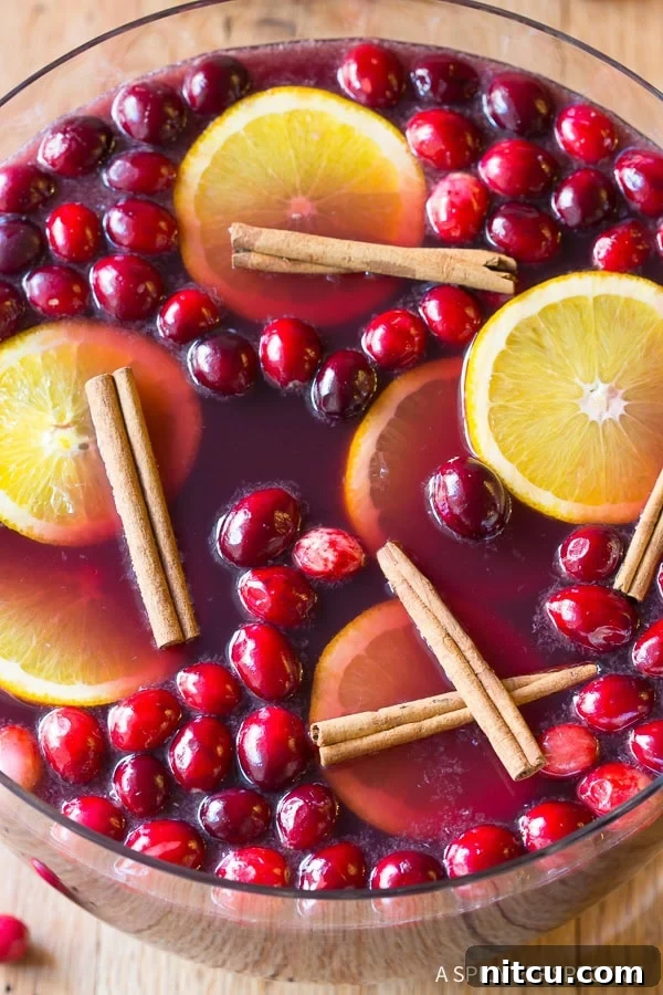 Festive Wine Medley 3 An overhead shot of a glistening punch bowl brimming with Holiday Wine Punch, adorned with vibrant cranberries, fragrant cinnamon sticks, and bright orange slices, ready for a festive gathering.