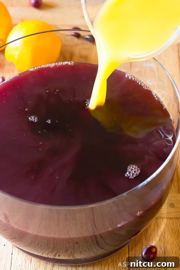 Festive Wine Medley 7 A vibrant stream of fruit juice being added to the red wine already in the punch bowl, showcasing the blend of flavors in the Holiday Wine Punch.