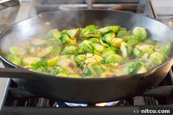 Braised sprouts simmering in a cast iron skillet with broth.