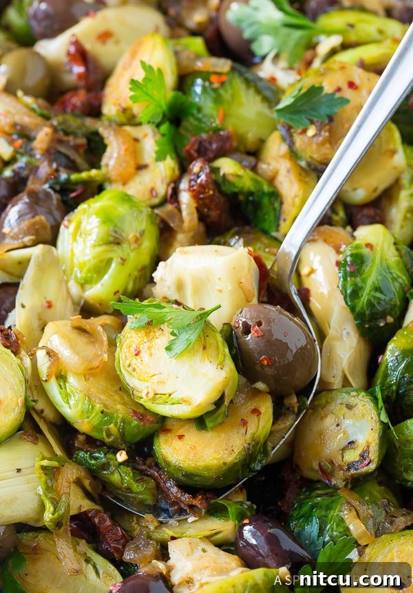 Metal spoon scooping up a servings of baised brussels sprouts with sun-dried tomatoes, greek olives, artichoke hearts and fresh chopped parsley, ready for plating.
